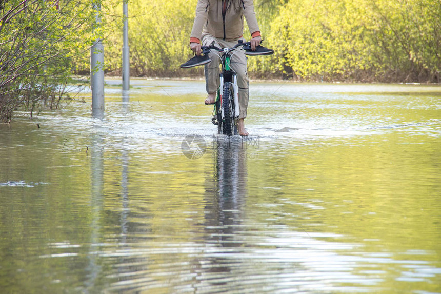 赤脚骑自行车的人试图在春天的洪水中克服随着河水冲破河岸图片
