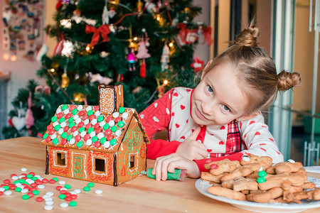 可爱的小女孩用灯光和圣诞树的釉面装饰姜饼屋图片