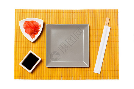 黄色竹席背景上带筷子的空灰色方形盘子图片