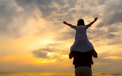 海边沙滩上夕阳背景下爸肩上小女孩的剪影图片
