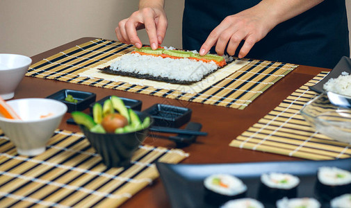 厨师手将食材放在米饭上制作寿司图片
