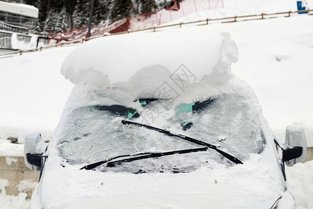 汽车在大雪后覆盖着厚的雪层的街道上极端暴风雪后果车辆挡风玻璃与冻图片