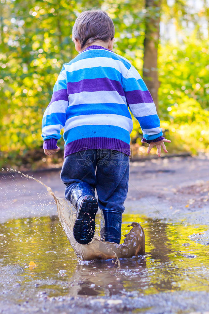 一个小男孩在水坑里跳一个穿着橡胶靴的男孩快乐的童年雨后的水坑温暖的夏日傍图片