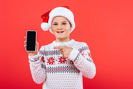戴着圣诞帽的微笑孩子用手指着智能手机的正面图背景图片