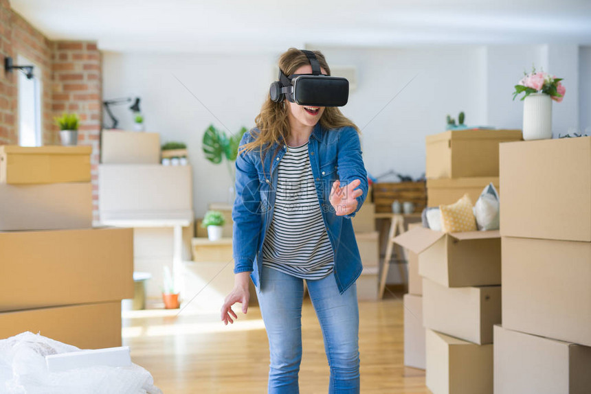 身戴虚拟现实眼镜的金发年轻女金发女孩在纸板盒上玩模拟游戏图片