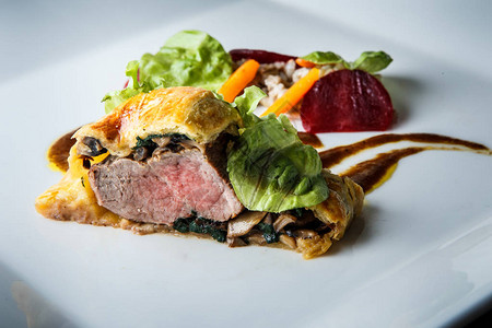 用蘑菇和菠菜在白色餐厅盘子上装饰沙拉叶和棕色酱汁的面团肉烤图片