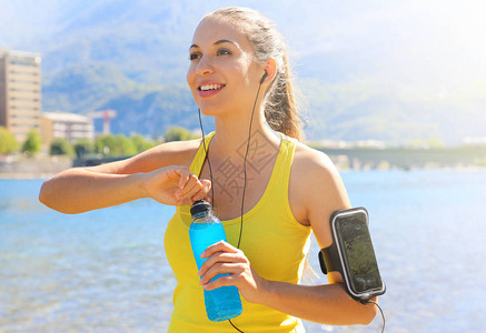拥有智能手机开源饮料瓶臂带的快乐女运动员在日常训练后图片