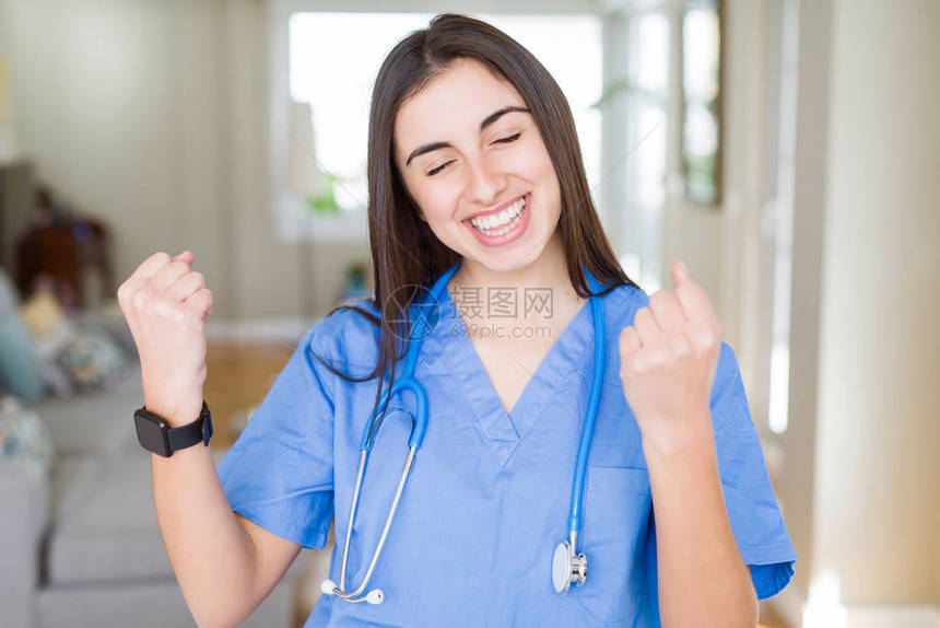 在诊所穿着制服和听诊器的漂亮年轻护士女人非常高兴和奋地做着胜利者的手势图片