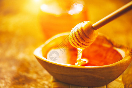 蜂蜜从木碗中的蜂蜜勺滴下从木蜂蜜勺特写中倒出的健图片