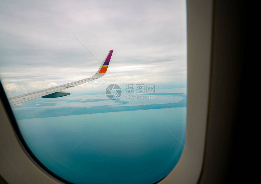 飞机翼在城市上空飞机在蓝天上飞行从飞机窗口的风景与白云天空和蓝色的商业航空公司飞行热带上图片