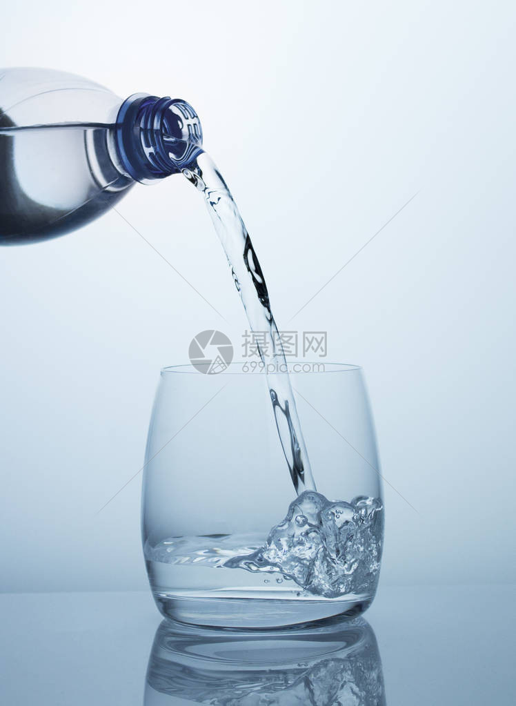 干净新鲜凉爽的饮用水从蓝色塑料瓶流入透明带美丽气泡的大肚玻璃玻璃中带有图片