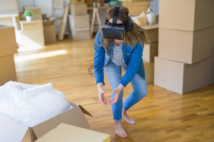身戴虚拟现实眼镜的金发年轻女金发女孩在纸板盒上玩模拟游戏图片