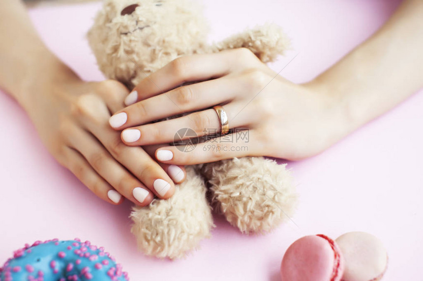 戴着婚戒的妇女手和修指甲的美甲妇女握着Teddy熊和粉红背景特图片