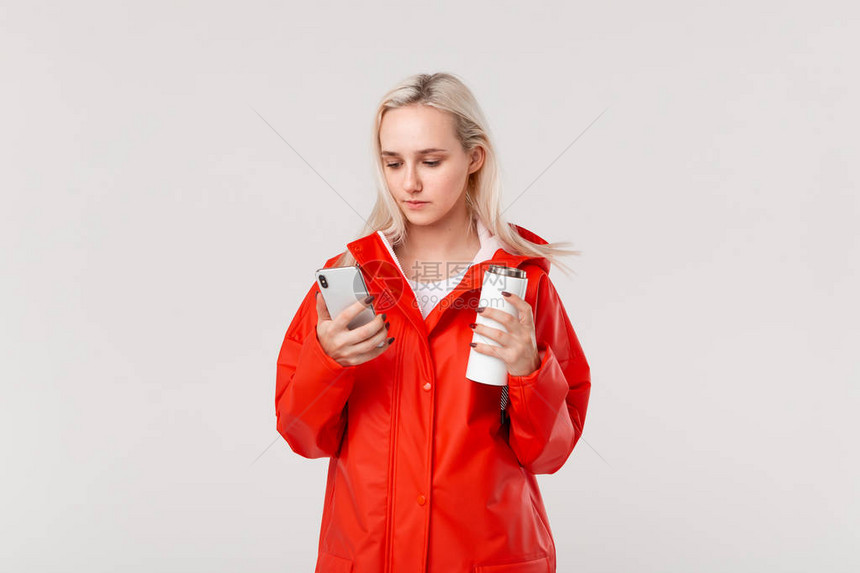 身穿红色雨衣的金发美女拿着带热饮料的白色保温杯图片