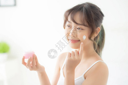 美丽的年轻亚洲女人快乐地将奶油或乳液与保湿霜涂抹在皮肤上图片