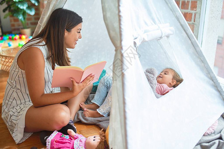 美丽的老师读书给金发女小孩看书躺在幼儿园小图片