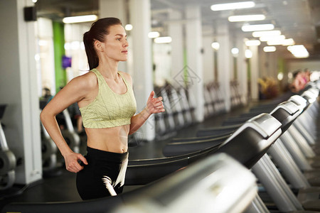 在空体操场复制空间的心胸锻炼期间在跑步机上运行的流汗年轻女图片