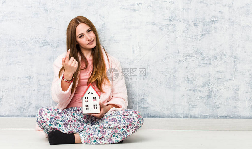 年轻caucasian女人拿着房子的图标用手指着你好像邀图片