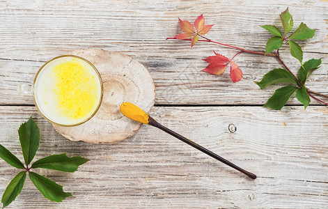 杯用牛奶和姜黄在木制基板上旁边是一把姜黄汤匙常春藤叶子在一个图片