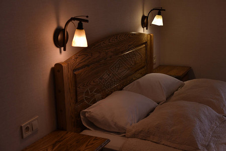 酒店房间的床和枕头一张带木制床头板和两个橱柜和落地灯的床白天或晚上的酒店睡觉和放松的地方白色枕套中背景图片