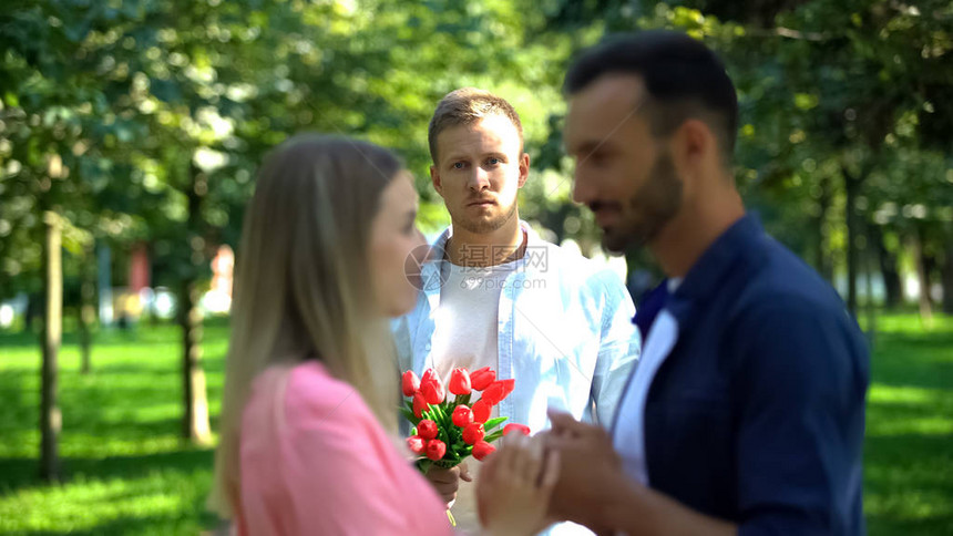带着鲜花的失望的男人看着女朋友和另一图片