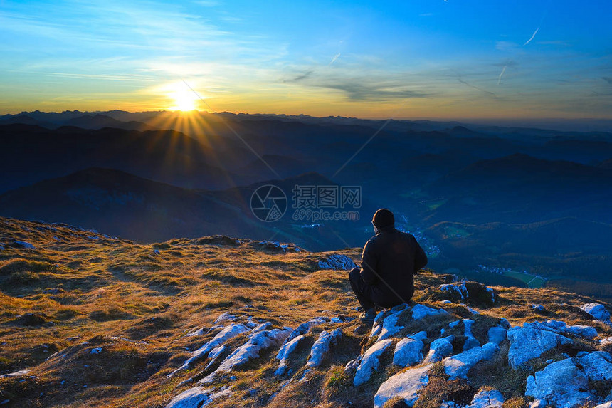 穿着黑色户外衣服的人坐在阿尔卑斯山脉破碎的岩石峰顶上观图片