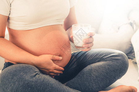 快乐的孕妇在家里用玻璃喝牛奶背景图片
