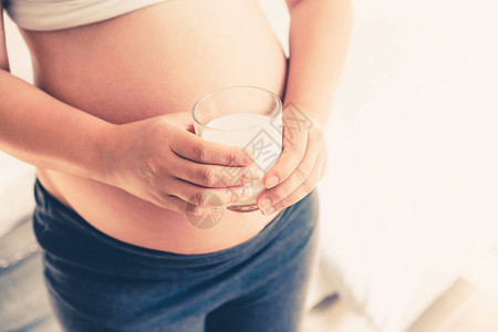 快乐的孕妇在家里用玻璃喝牛奶背景图片
