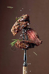 烤肋眼牛排配上棕色背景的迷迭香叉子上的牛排撒上图片