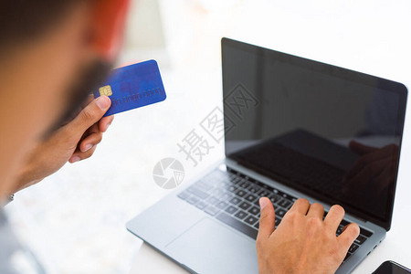 使用笔记本电脑在网上购物时将信用卡作付款计量仪的男子图片