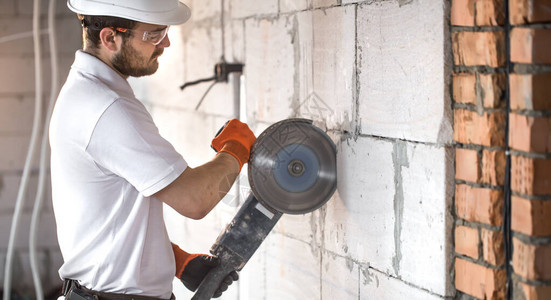 工业建筑商与专业角磨机一起切割砖块和建造内墙施工现场的专业人士电工背景图片