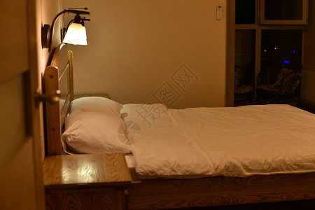 酒店房间的床和枕头一张带木制床头板和两个橱柜和落地灯的床晚上酒店睡觉和放松的地方白色枕套中背景图片