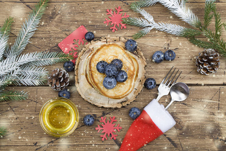 自制煎饼配蓝莓蜂蜜早餐圣诞树枝和木上的雪冬天早餐的美味甜点顶视图图片
