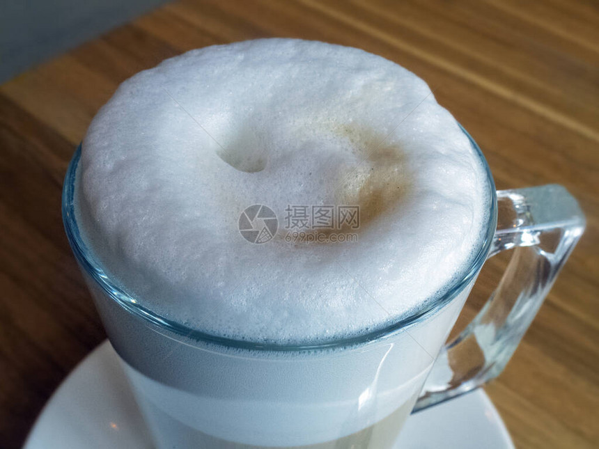桌子上的拿铁咖啡杯特写咖啡表面的搅打牛奶形成浓郁的泡沫泡沫从图片