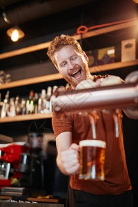英俊的caucasian酒吧男招待站在酒吧里喝啤酒图片