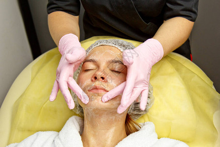 概念美容师美容师的手把奶油涂在女人的脸上美容师将奶油涂图片