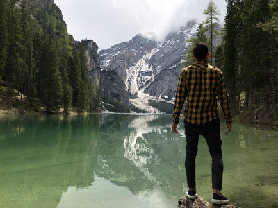 在白天森林覆盖的山中站在湖岸边的男旅行图片