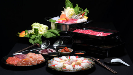 火锅涮锅鲜肉片海鲜和黑色背景蔬菜图片
