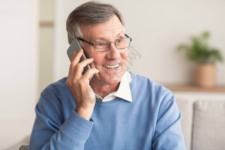 电话快乐的老人坐在家里的沙发上用手机说话图片