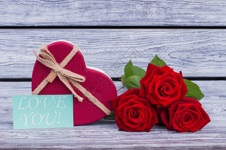 心形礼品盒和红玫瑰情人节礼物鲜花和带有铭文的纸卡爱你在木制背景上图片