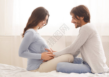 微笑的男人温柔地抚摸怀孕妻子的肚子图片
