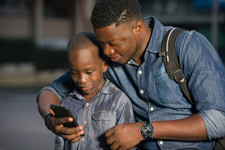 父亲和儿子坐在街上等车看着手机图片
