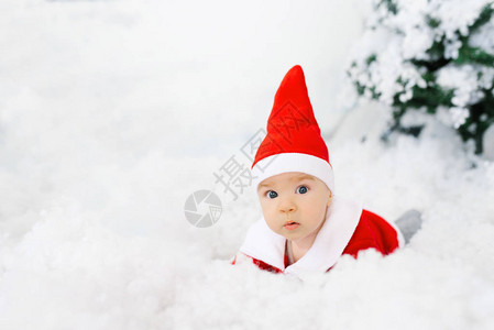 一个穿着圣诞老人西装和帽子的小孩躺在雪地上复制空间圣诞图片