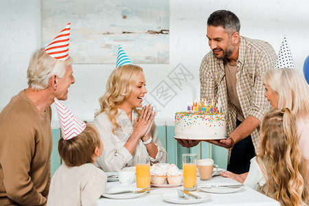 男人笑着拿生日蛋糕的生日蛋糕与蜡烛在幸福的家庭附近图片