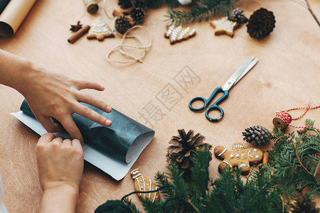 包装圣诞礼物的概念用黑纸和松枝锥姜饼线肉桂剪刀在乡村木桌上包裹图片