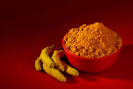 红色背景中红碗中的干姜黄粉和根或树皮高清图片