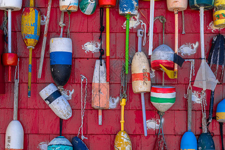 美国马萨诸塞州波士顿木制红墙背景上悬挂的各种五颜六色的鱼浮标导航设备和旅行背背景图片