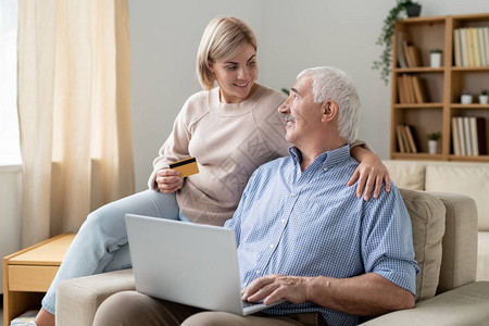 带着信用卡的漂亮临时工妇女看着她退休后的父亲拿着笔记本电脑背景图片