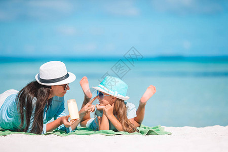 年轻的母亲在海滩上给女儿鼻子涂防晒霜紫外线辐图片