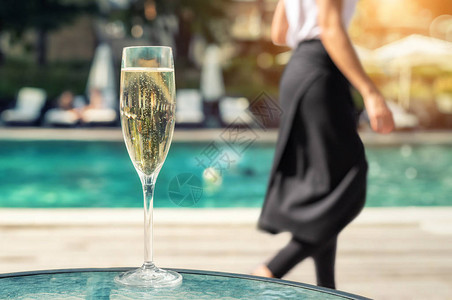 度假期间在豪华度假酒店的池畔特写白色香槟或普罗赛克玻璃与上升的气泡的起泡酒与室外的蓝色水池背景黑裙子背景图片